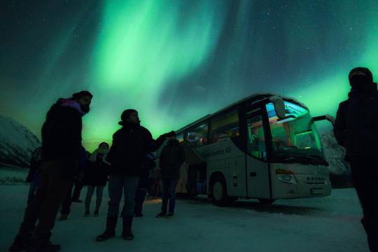 Guests outside the bus with northern lights in the background