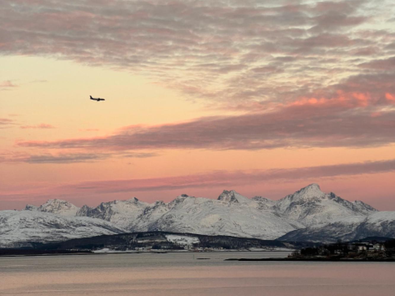 Et fly flyr over snøkledde fjell.