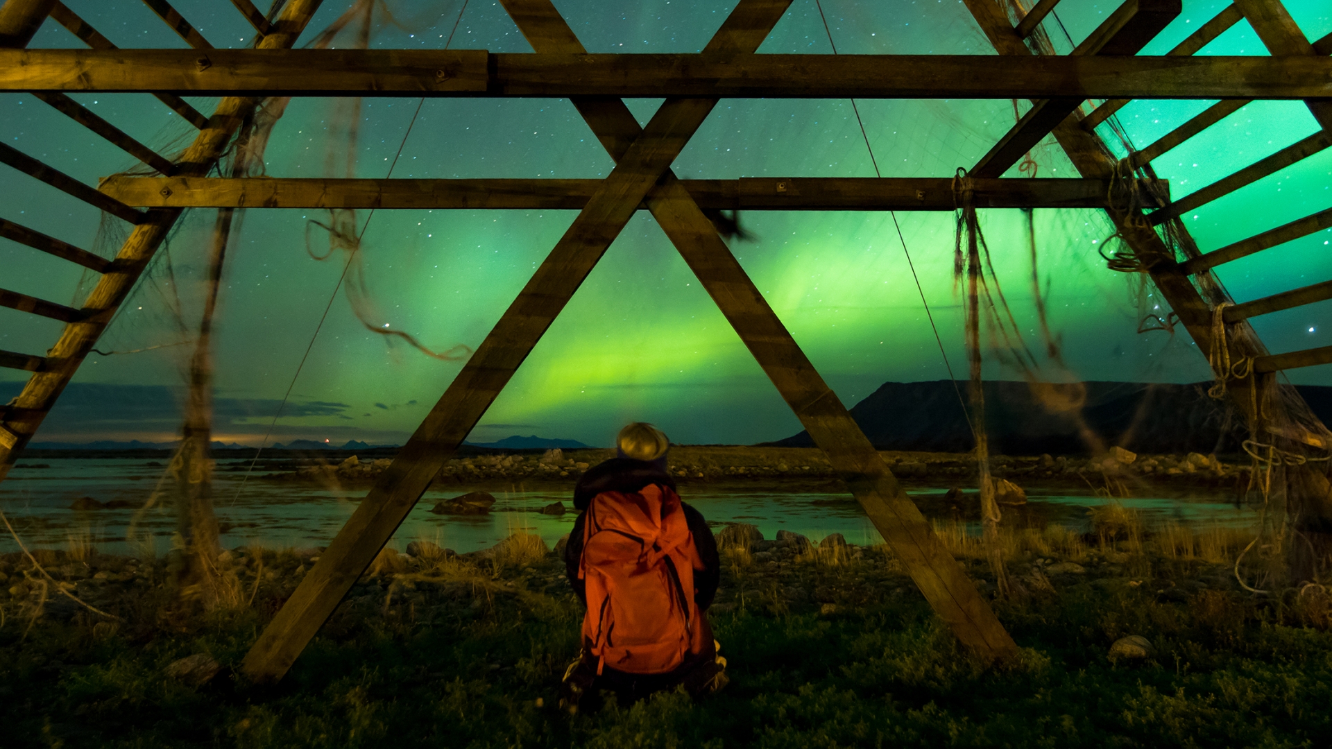 Woman sitting by the ocean watching the Northern Lights