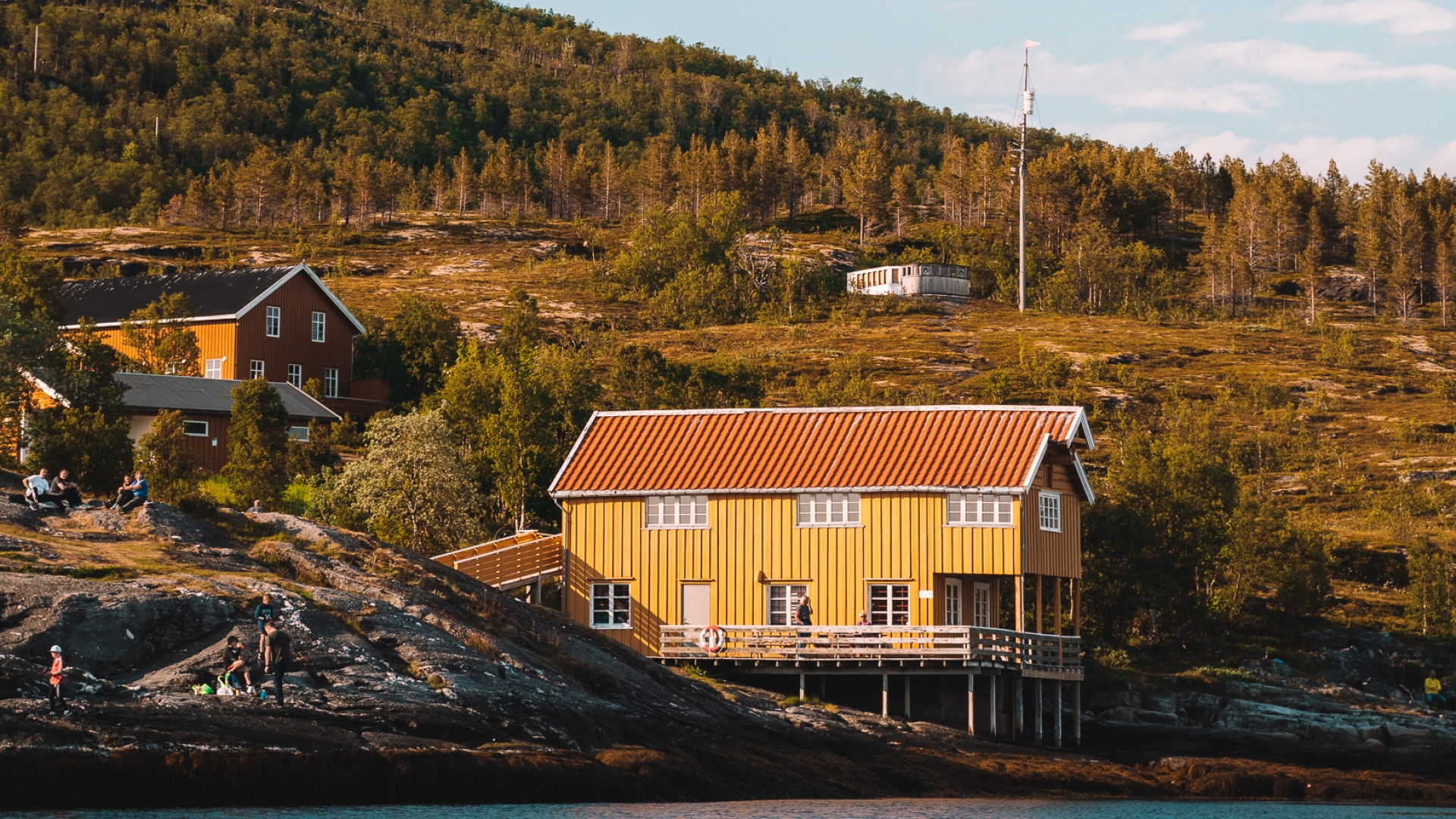 Mennesker nyter sola ved Hellastua på Hella utenfor Tromsø