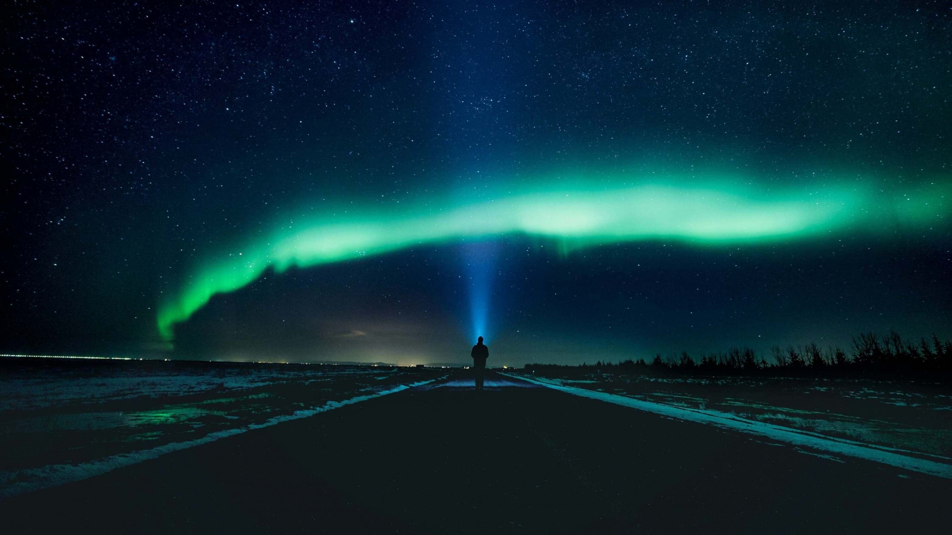 Person walking on the road with a head torch looking up at the northern lights