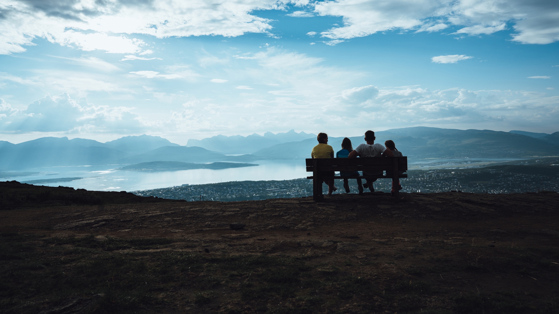 Family sitting on a bench on the top of Mount Storsteinen watching Tromsø city