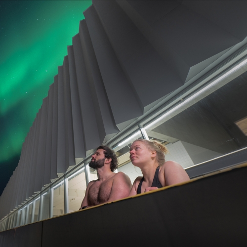 Man and woman in outdoor pool under the Northern Lights