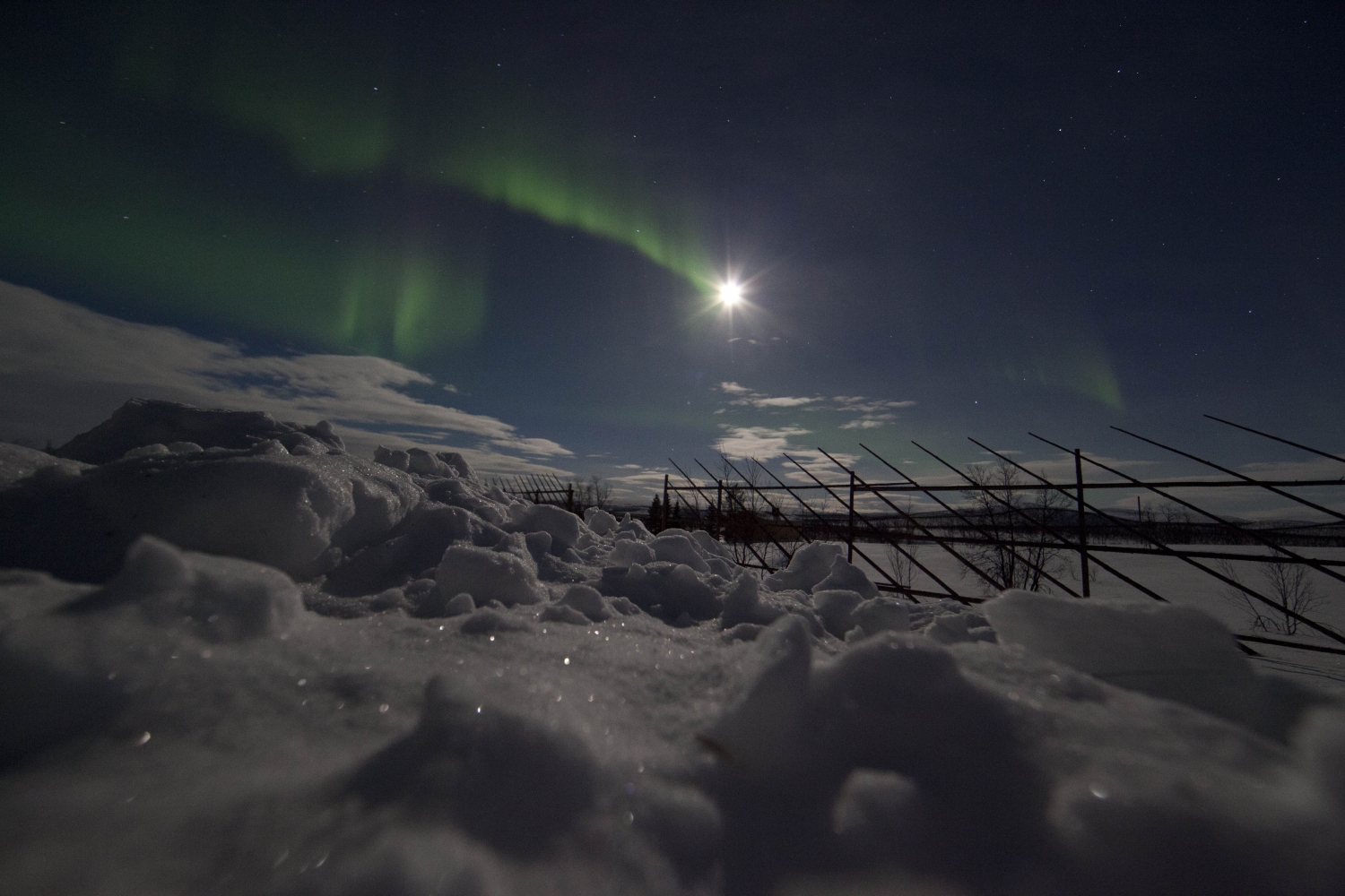 Northern lights over snow, moonlight in the background