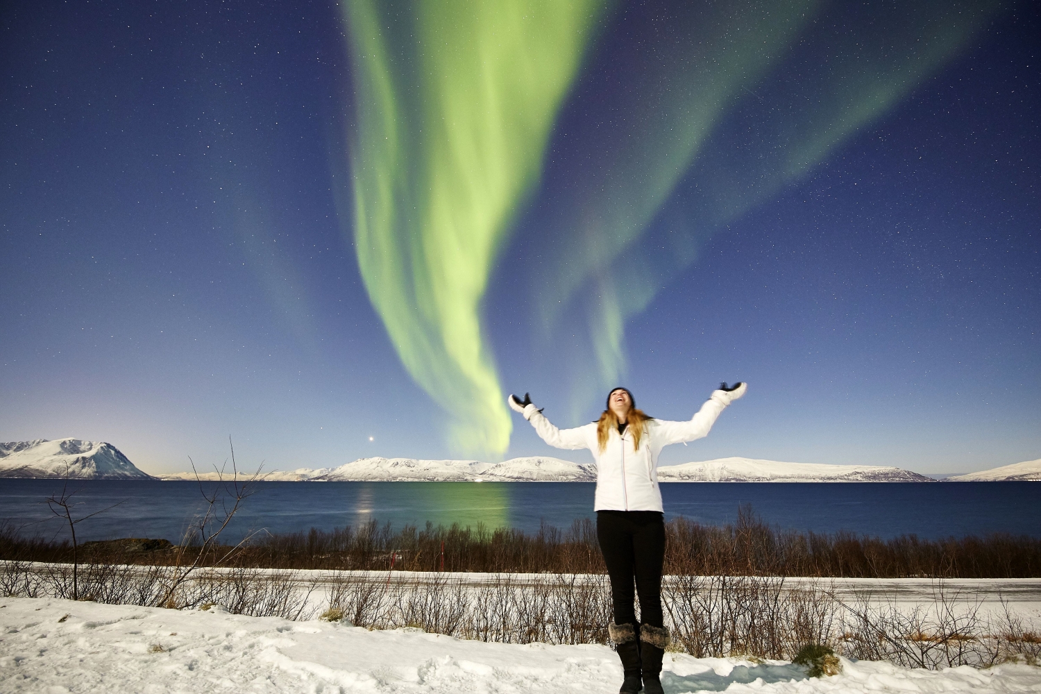 a woman standing with her arms up and looking at the sky where the northern lights are