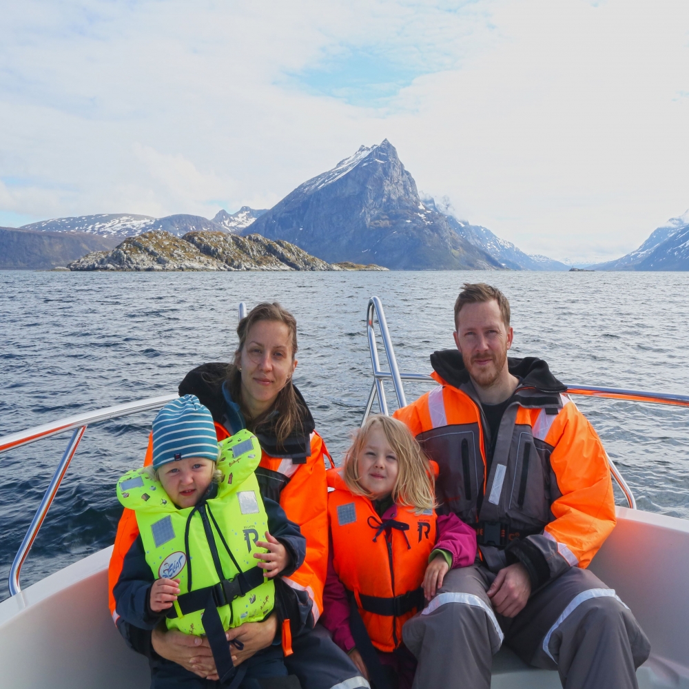 Familie ombord på båt, fjell og hav i bakgrunnen