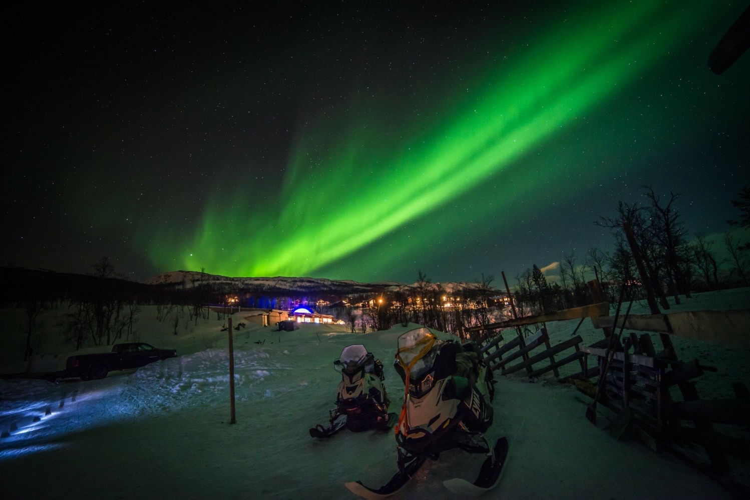 Northern lights above Arctic winter landscape, and snowmobiles