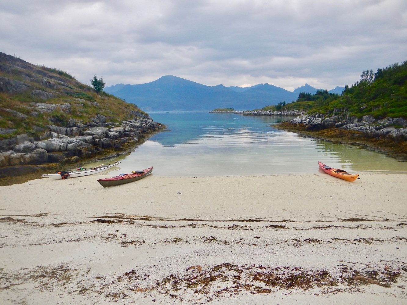 Kayaks at a sandy beach, mountains in the background