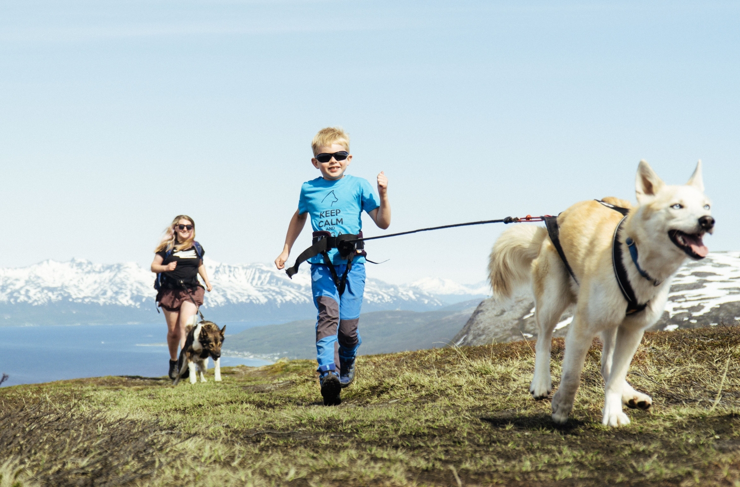 Woman and child running with huskies on top of the mountain