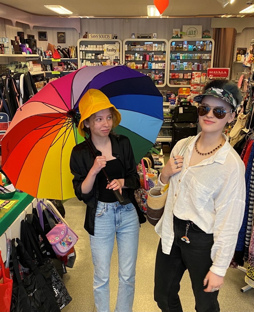 To people trying some clothes, hats and a rainbow umbrella.