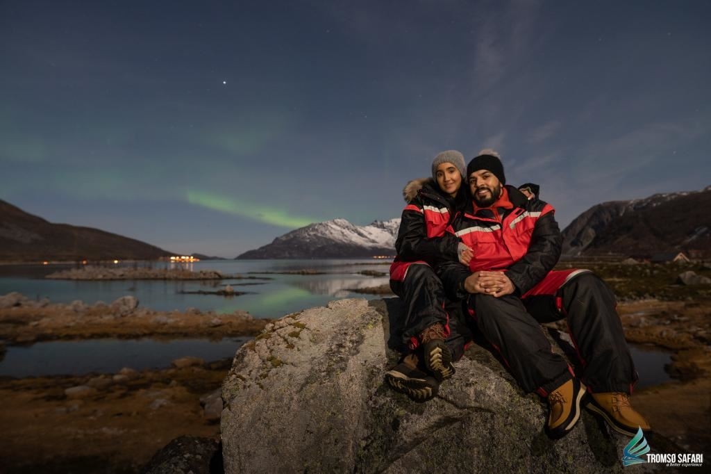 two people enjoying the northern lights by the fjord