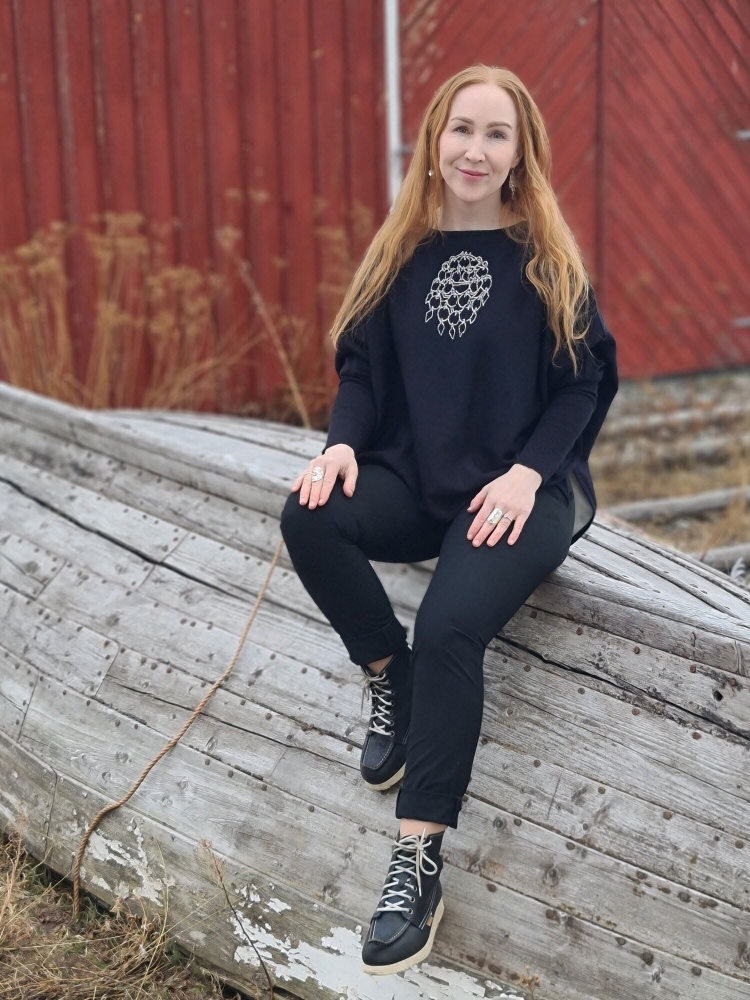 Jente som sitter på en gammel trebåt i samisk design genser