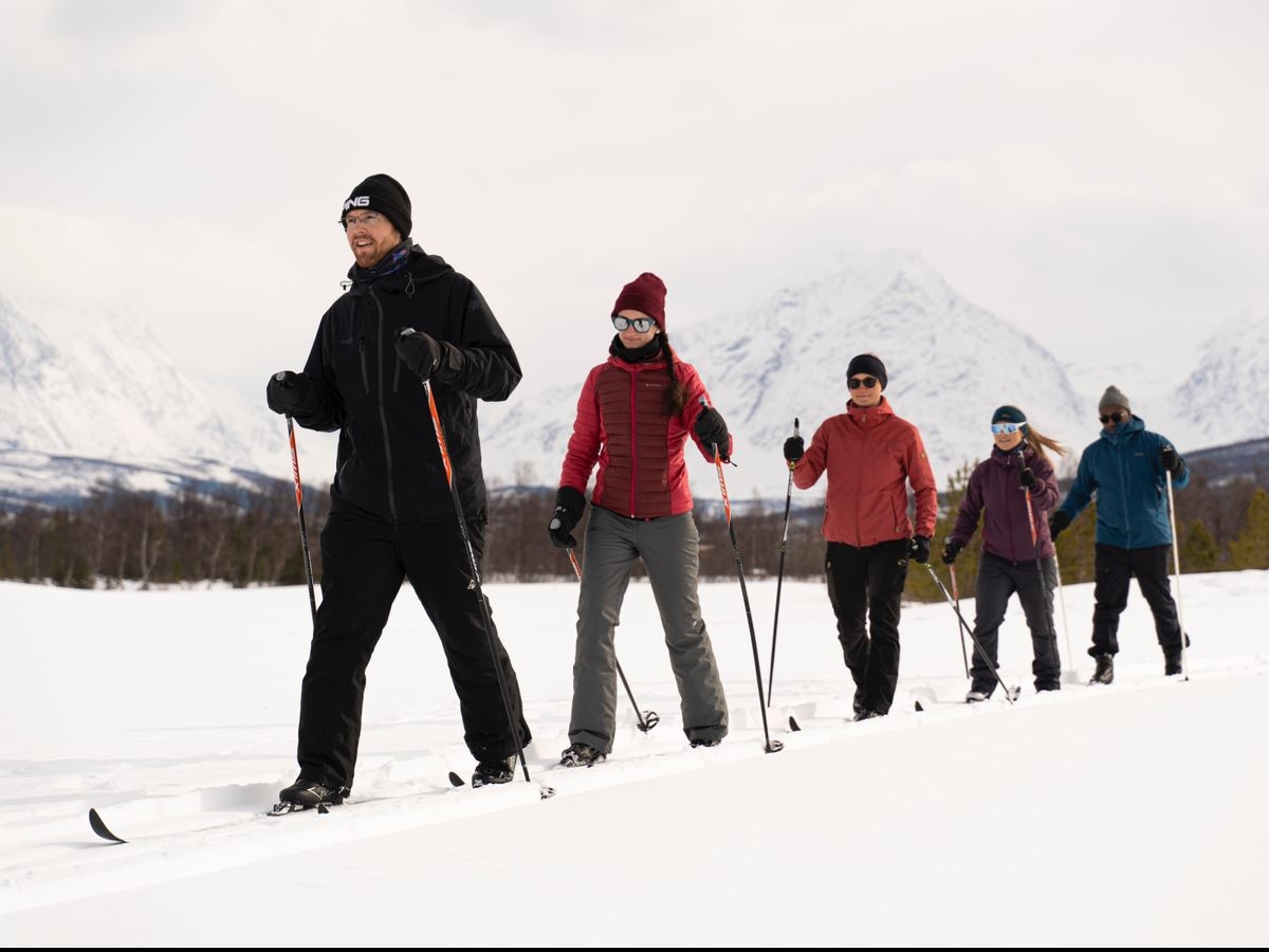 fem personer som går på ski med Lyngsalpene i bakgrunnen
