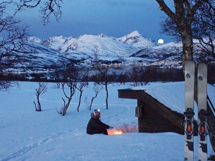 Moon behind mountains whilst person enjoying bonfire in the snow