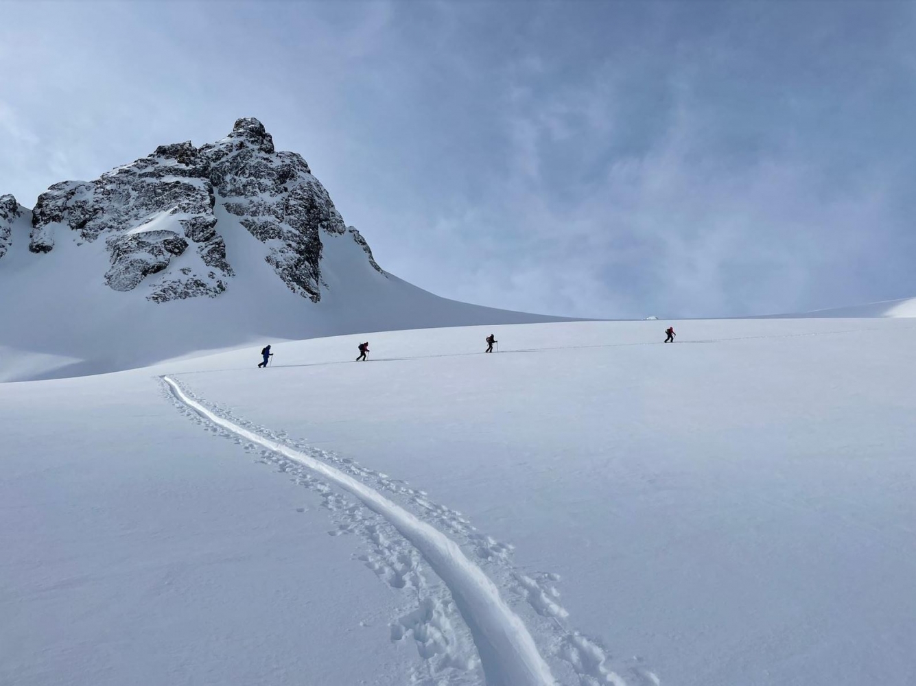 Four people on their way up a mountain on skiis