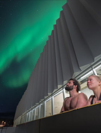 Man and woman in a pool under the Northern Light sky