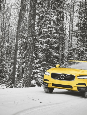 yellow car driving on a winter road with trees in the background