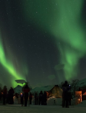 people watching the northern lights dance over the camp site