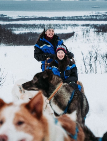 Two guests dog sledding with happy huskies