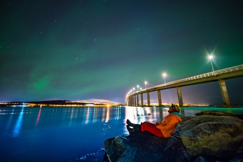 Woman watching the Northern Lights by the bridge to Kvalyøya in Tromsø