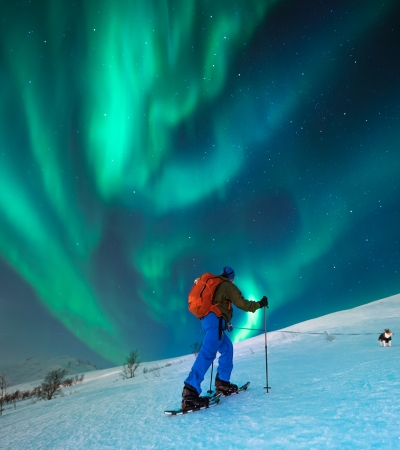 Man snowshoeing under the Northern Lights