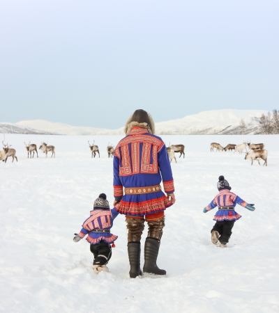 Mann og barn i tradisjonelle samiske klær med reinsdyr i bakgrunnen