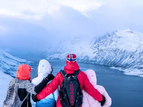 Four guests overlooking a snow-covered fjord and mountains during a winter tour in Northern Norway.