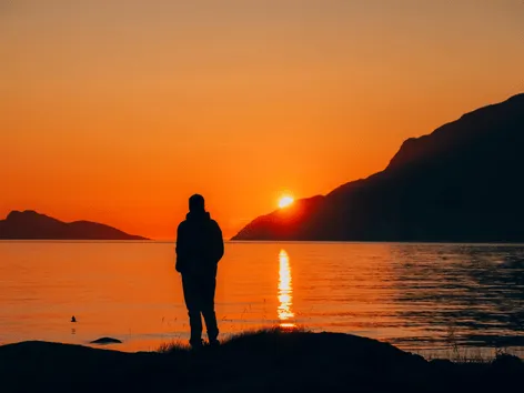 Silhuett nyter utsikten og midnattssola