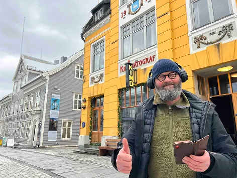 En person som hører på en audioguide og gir tommel opp