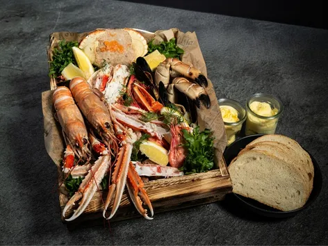 Different seafood ingredients in a box with butter and bread in the background