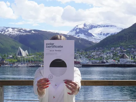 Woman holding a Polar Certificate from Visit Tromsø-Region in the summer with the Arctic Cathedral and Tromsdalstinden in the background.