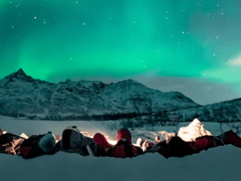 Gjester som ligger ved et bål og ser på nordlyset