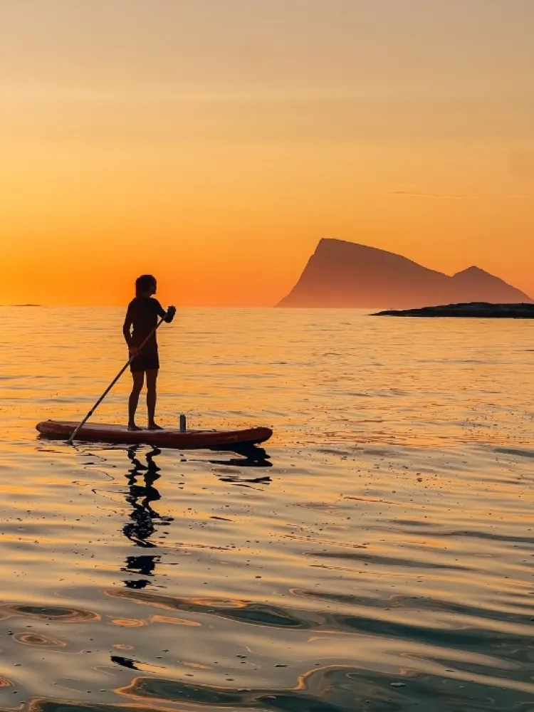 A woman Stand Up Padling under the midnight sun in the Tromsø region