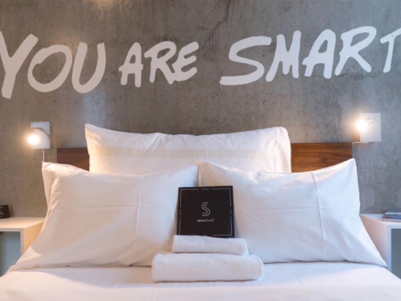 Seng i et hotellrom på Smarthotel. "Your are smart" står skrevet på veggen.