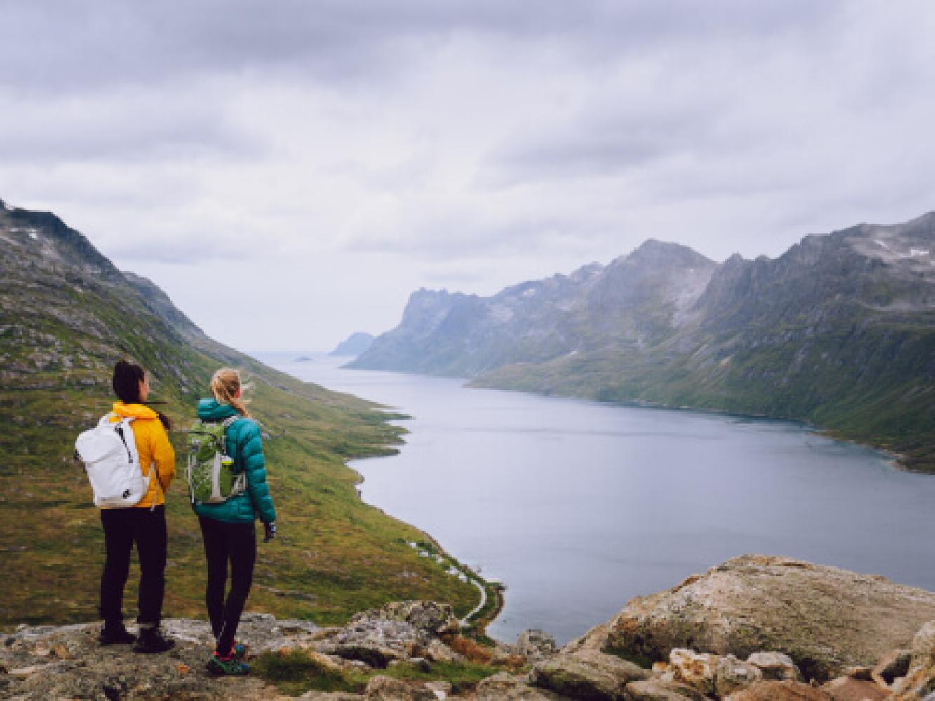 To personer står på et fjell og ser utover et landskap.