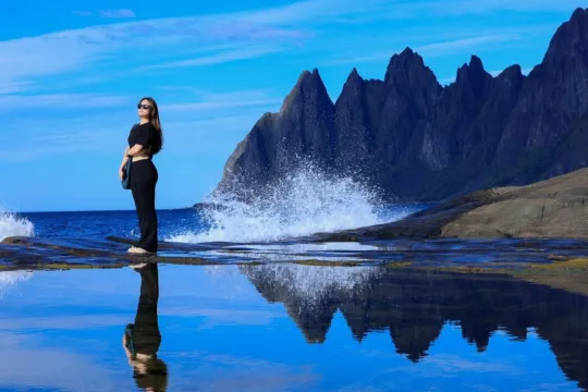 Person poserer ved kysten med fjell i bakgrunnen