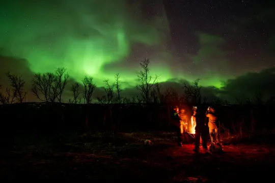 Guests around a bonfire and Northern lights