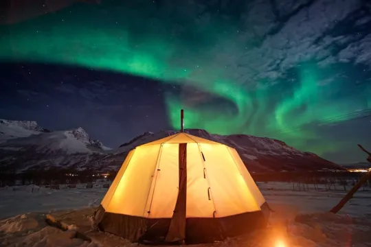 Glødende telt i snødekt landskap under nordlys.
