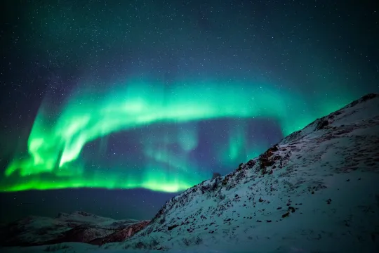 The Northern Lights show themselves behind a mountain clad in snow