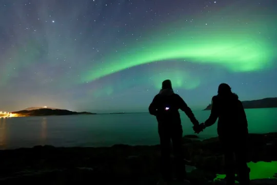 Gjester står ved fjorden og ser på nordlyset som danser over hodene deres