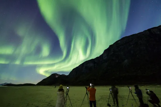 Gjester ser på nordlyset som viser seg bak et stort fjell