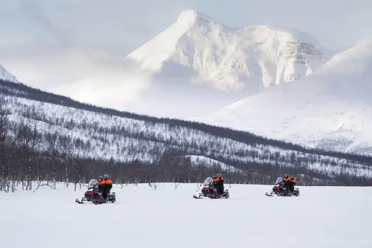 Three snow scooters drive past massive and beautiful mountains