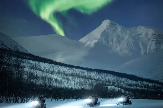 Guests drive snow scooters with the Aurora above their heads