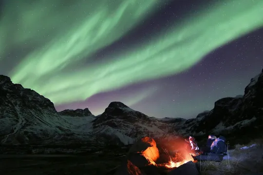 Bålkos i snødekt fjellandskap under nordlys 