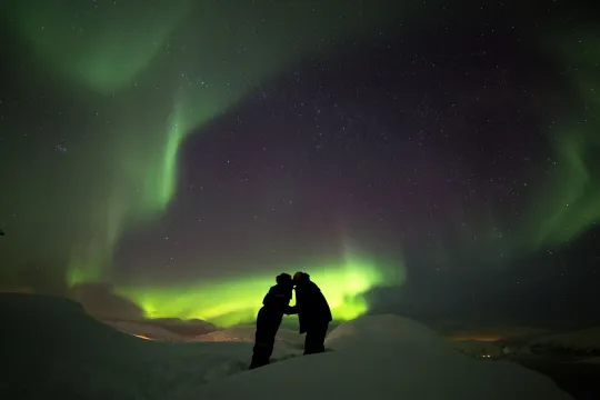 Two guests kissing under the northern lights