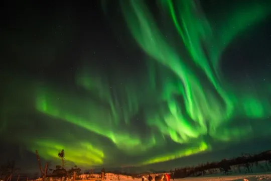 Guests around a campfire under the Northern lights