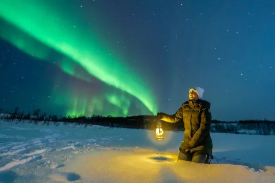 A person holding a lamp under the Northern Lights