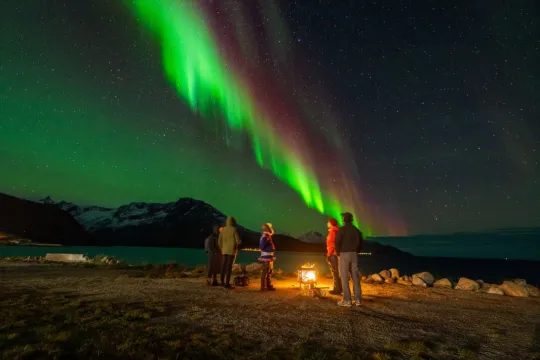 Guests sit around the fire, watching the Northern Lights dance overhead