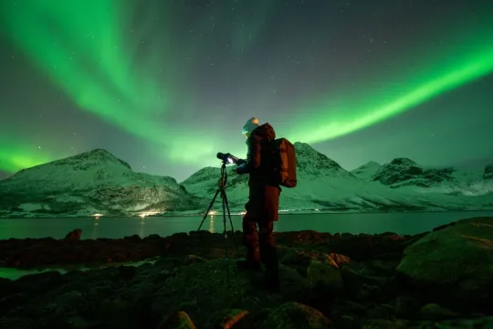 A photographer points the camera up at the Northern Lights, which creates an arch overhead