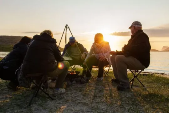 A group of guests sitting around a bonfire by the shoreline